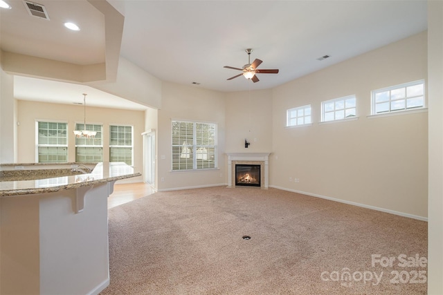 unfurnished living room with ceiling fan with notable chandelier, light carpet, and a wealth of natural light