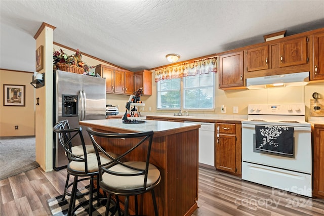 kitchen with white appliances, wood-type flooring, a textured ceiling, ornamental molding, and a breakfast bar