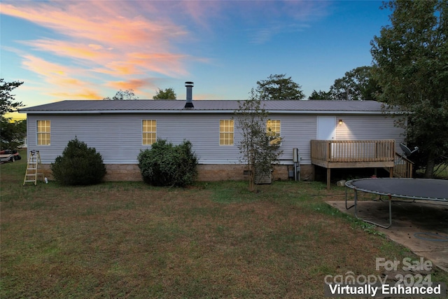 back house at dusk with a wooden deck and a lawn