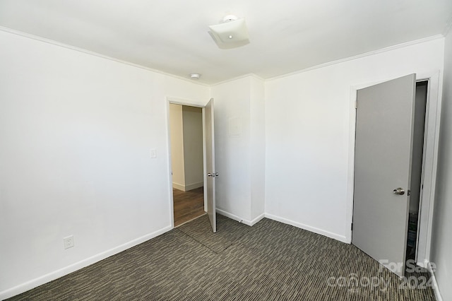 empty room with crown molding and dark colored carpet