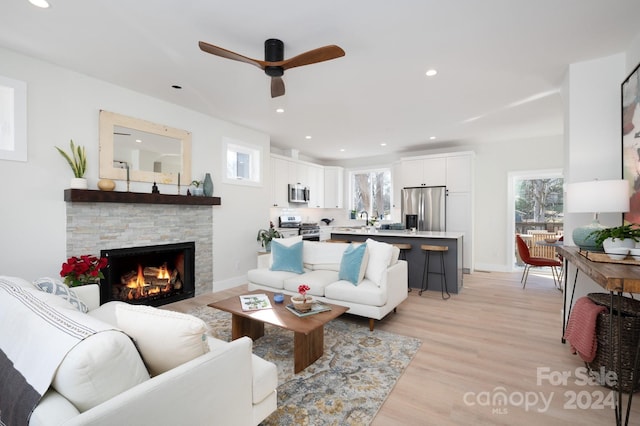 living room featuring a stone fireplace, ceiling fan, sink, and light wood-type flooring