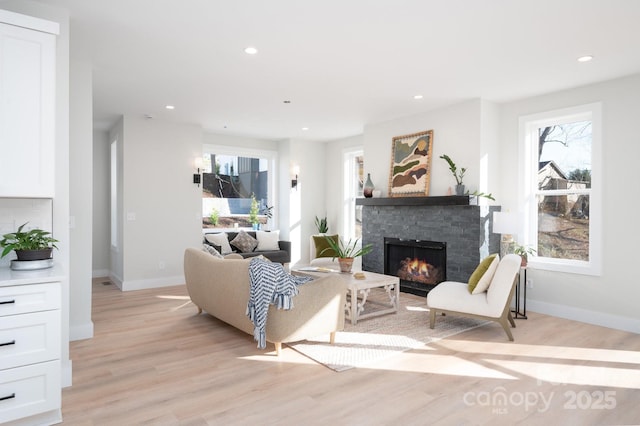 living room featuring a stone fireplace, plenty of natural light, and light wood-type flooring