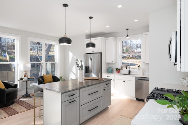 kitchen with stainless steel appliances, sink, pendant lighting, white cabinetry, and a kitchen island