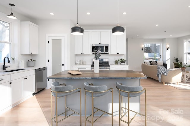 kitchen with white cabinetry, sink, hanging light fixtures, a kitchen island, and appliances with stainless steel finishes