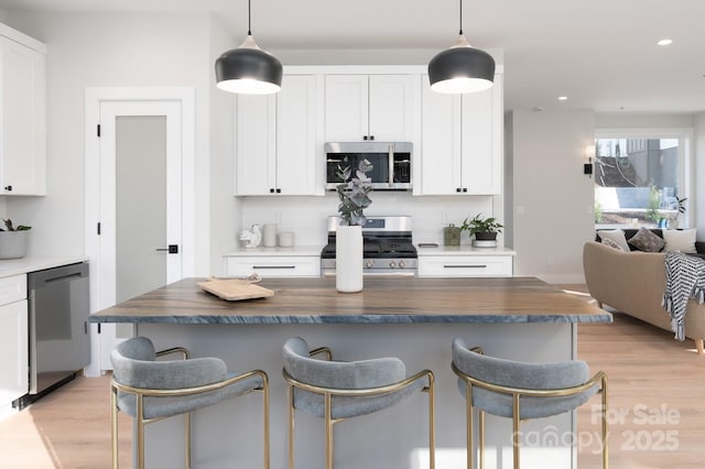 kitchen with wooden counters, decorative light fixtures, stainless steel appliances, and white cabinetry