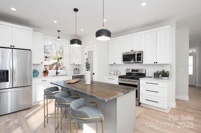 kitchen with stainless steel appliances, a kitchen island, backsplash, decorative light fixtures, and white cabinets