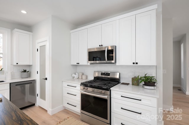 kitchen with white cabinets, decorative backsplash, light hardwood / wood-style floors, and stainless steel appliances