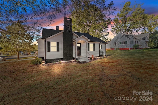 back house at dusk featuring a lawn