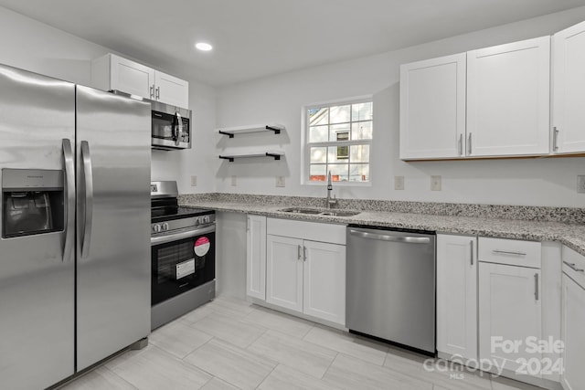 kitchen featuring appliances with stainless steel finishes, white cabinets, sink, and light stone counters