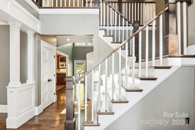 stairs with hardwood / wood-style floors, a high ceiling, and decorative columns