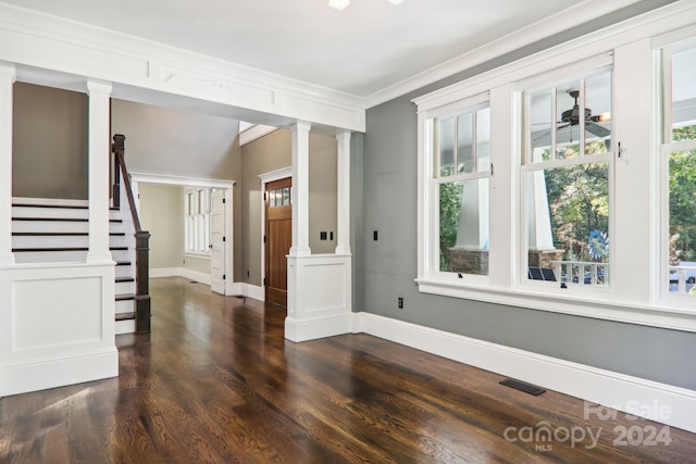 empty room with dark wood-type flooring, crown molding, and decorative columns