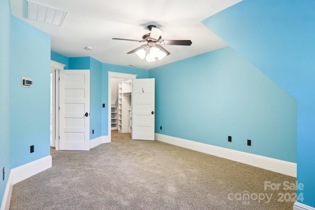 unfurnished bedroom with carpet flooring, a walk in closet, a closet, and ceiling fan