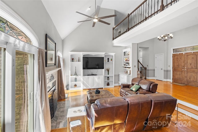 living room with high vaulted ceiling, ceiling fan with notable chandelier, and light wood-type flooring