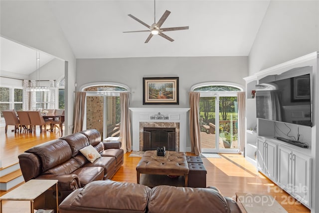 living room with ceiling fan, high vaulted ceiling, a premium fireplace, and light wood-type flooring