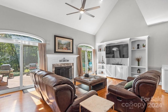 living room featuring ceiling fan, high vaulted ceiling, light hardwood / wood-style flooring, and a fireplace