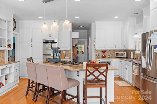 kitchen featuring a kitchen island, light hardwood / wood-style floors, stainless steel appliances, white cabinets, and a breakfast bar area