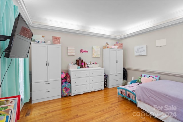 bedroom with crown molding, a tray ceiling, and light wood-type flooring