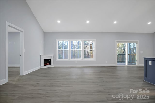 unfurnished living room with recessed lighting, wood finished floors, baseboards, vaulted ceiling, and a lit fireplace