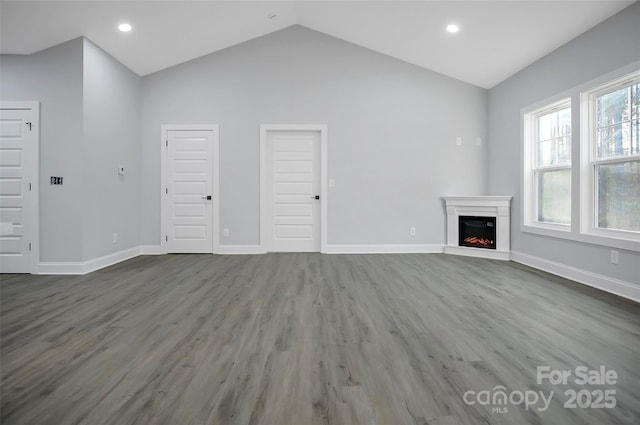 unfurnished living room with lofted ceiling, a warm lit fireplace, baseboards, and wood finished floors