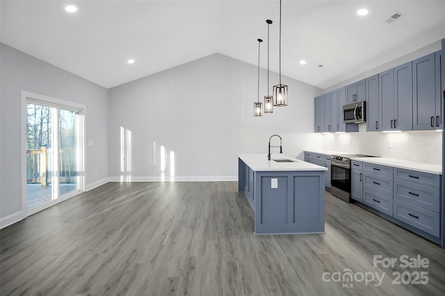 kitchen with lofted ceiling, appliances with stainless steel finishes, hanging light fixtures, a center island with sink, and light wood-type flooring