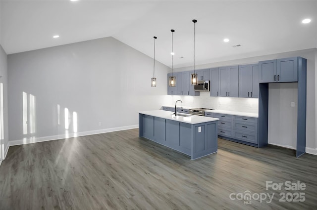 kitchen featuring light countertops, appliances with stainless steel finishes, vaulted ceiling, a sink, and wood finished floors