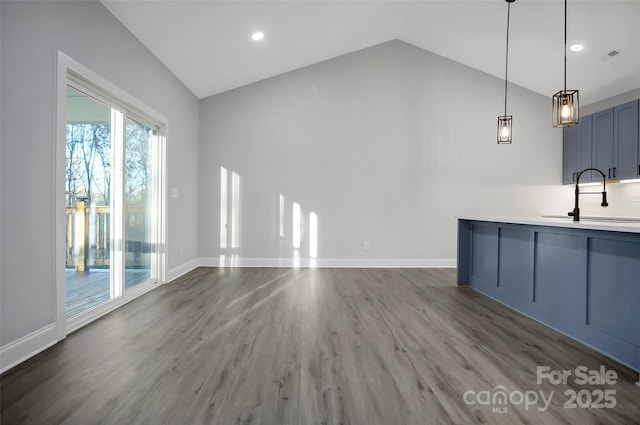 interior space with hanging light fixtures, vaulted ceiling, a sink, wood finished floors, and baseboards