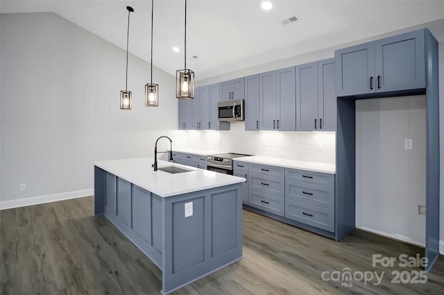 kitchen with pendant lighting, sink, appliances with stainless steel finishes, a center island with sink, and vaulted ceiling