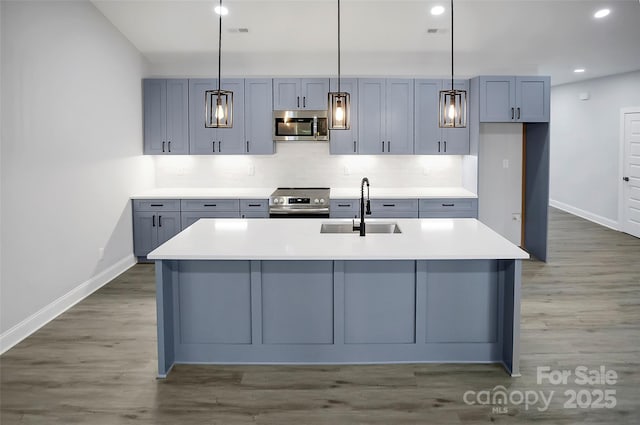 kitchen featuring sink, dark wood-type flooring, appliances with stainless steel finishes, a kitchen island with sink, and decorative light fixtures