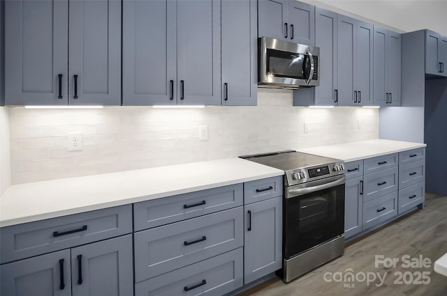 kitchen with appliances with stainless steel finishes, light countertops, backsplash, and light wood finished floors