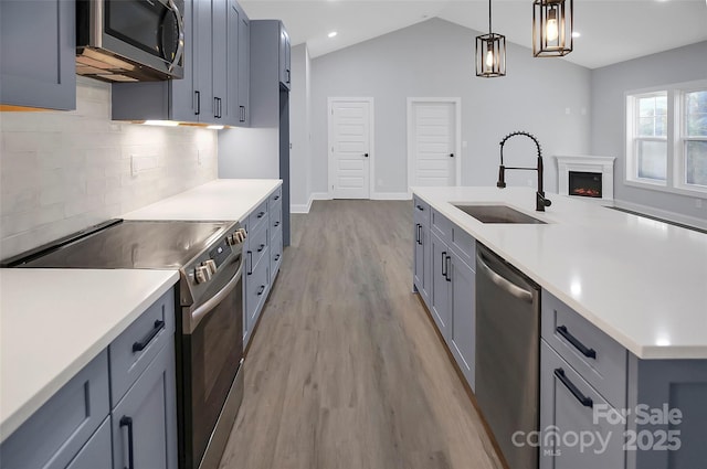 kitchen with a lit fireplace, stainless steel appliances, light countertops, light wood-type flooring, and a sink