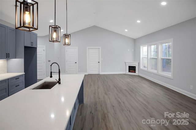 kitchen featuring lofted ceiling, dark wood-type flooring, a sink, baseboards, and a lit fireplace