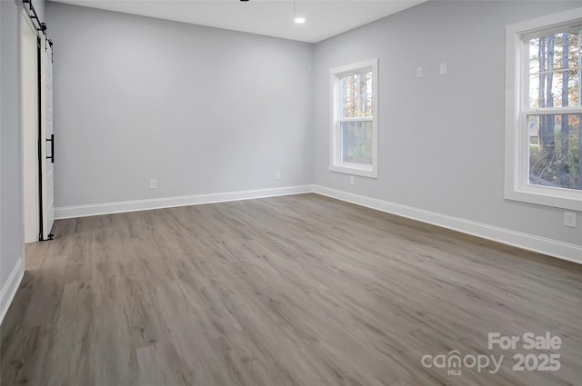 empty room featuring a barn door, recessed lighting, wood finished floors, a ceiling fan, and baseboards