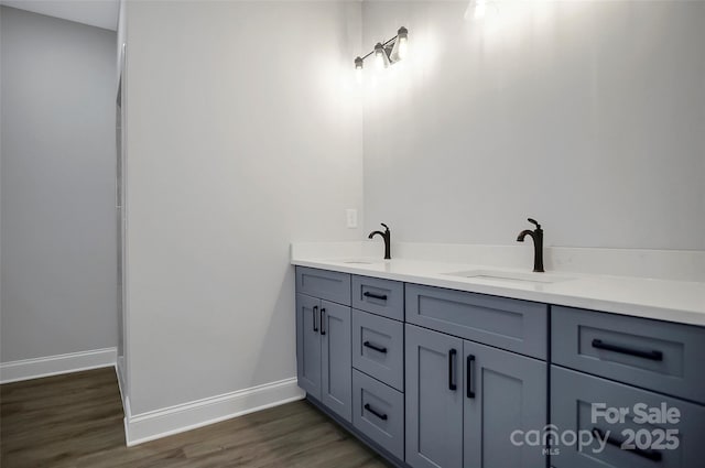 full bath with double vanity, a sink, baseboards, and wood finished floors