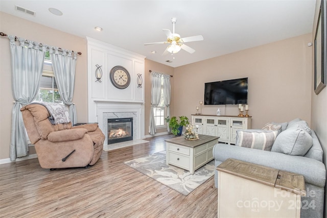 living area with light wood-style flooring, baseboards, visible vents, a ceiling fan, and a high end fireplace
