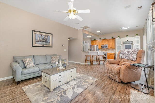 living room with a ceiling fan, baseboards, visible vents, and light wood finished floors