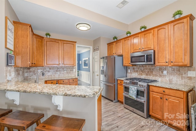 kitchen with light stone counters, stainless steel appliances, light hardwood / wood-style flooring, and kitchen peninsula