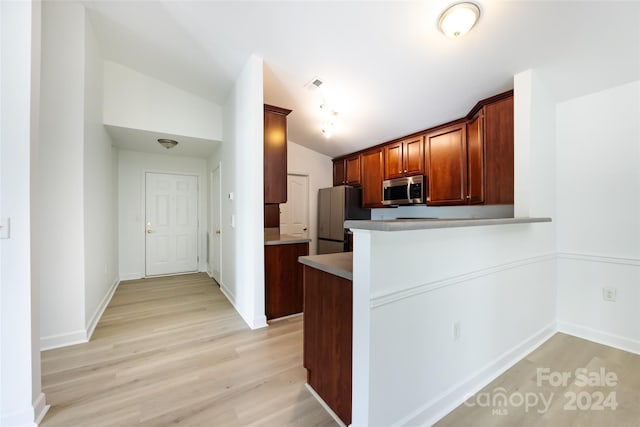 kitchen with light hardwood / wood-style flooring, stainless steel appliances, kitchen peninsula, and vaulted ceiling