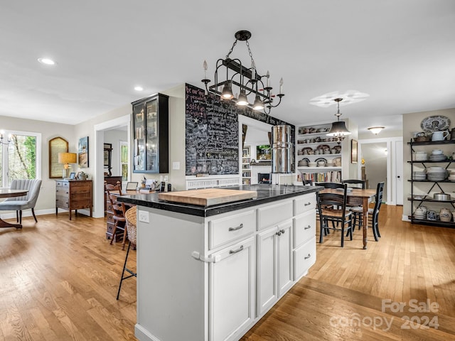 kitchen with white cabinetry, hanging light fixtures, a kitchen bar, a kitchen island, and light wood-type flooring