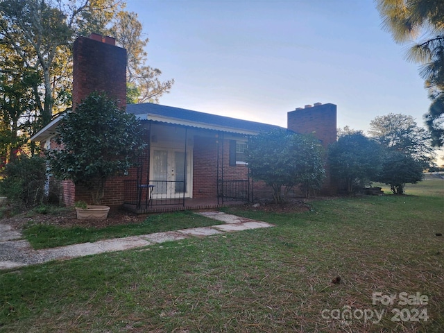 view of front of house with brick siding, french doors, a front lawn, and a chimney