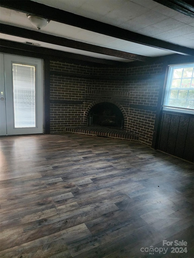 unfurnished living room with dark wood finished floors, a brick fireplace, and beamed ceiling