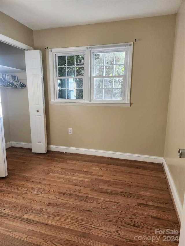 unfurnished bedroom featuring baseboards, wood finished floors, and a closet
