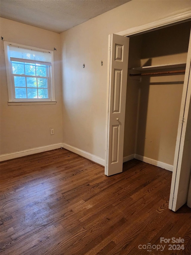 unfurnished bedroom featuring dark wood-type flooring, a closet, and baseboards