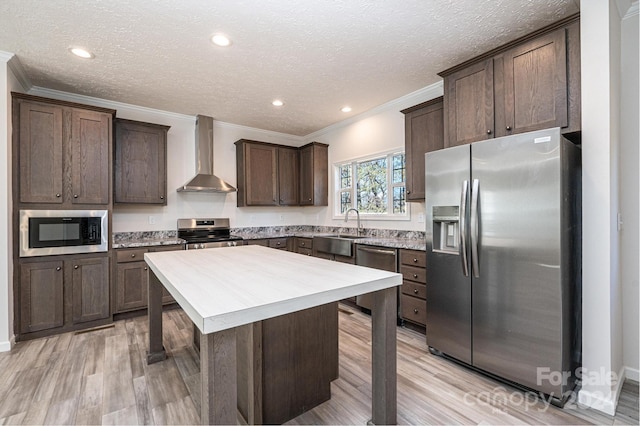 kitchen featuring wall chimney exhaust hood, stainless steel appliances, crown molding, light hardwood / wood-style flooring, and a kitchen island