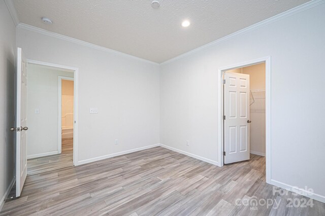 empty room featuring light wood-type flooring, a textured ceiling, and ornamental molding