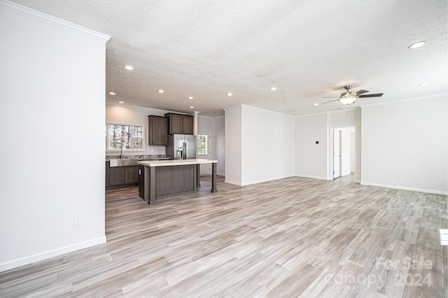 unfurnished living room featuring sink, light hardwood / wood-style flooring, ceiling fan, ornamental molding, and a textured ceiling