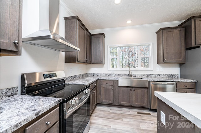 kitchen with ornamental molding, wall chimney exhaust hood, stainless steel appliances, sink, and light hardwood / wood-style floors