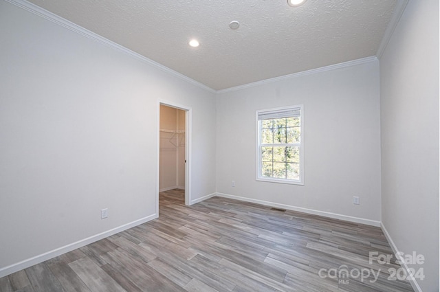 empty room featuring a textured ceiling, light hardwood / wood-style floors, and crown molding