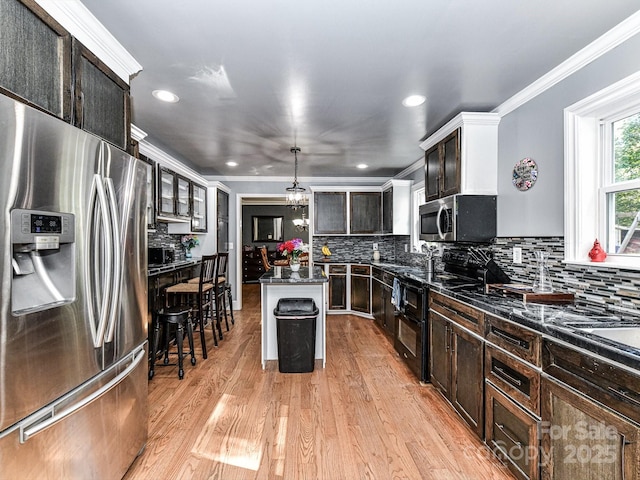 kitchen featuring appliances with stainless steel finishes, a center island, decorative light fixtures, dark brown cabinets, and a breakfast bar area