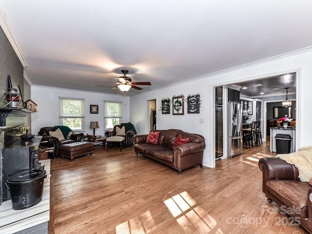 living room featuring a fireplace, ceiling fan with notable chandelier, ornamental molding, and light hardwood / wood-style floors