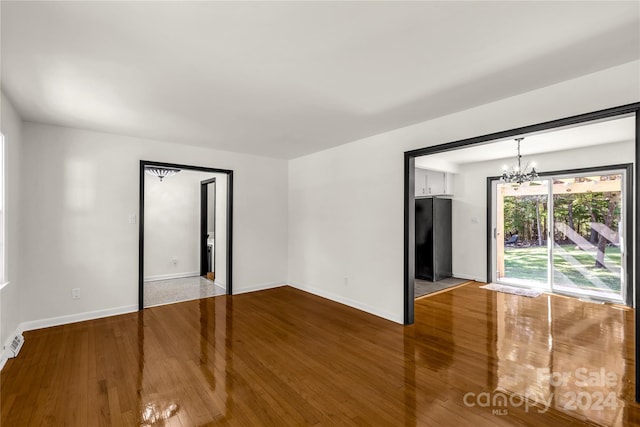 empty room featuring wood-type flooring and an inviting chandelier